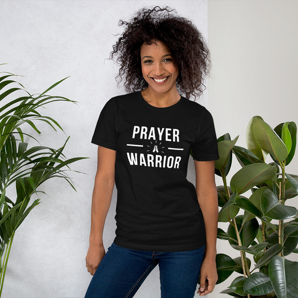 A woman wearing a black unisex t-shirt with "Prayer Warrior" written in bold white font.